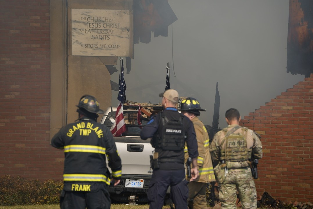 First responders stand behind a truck crashed into a building