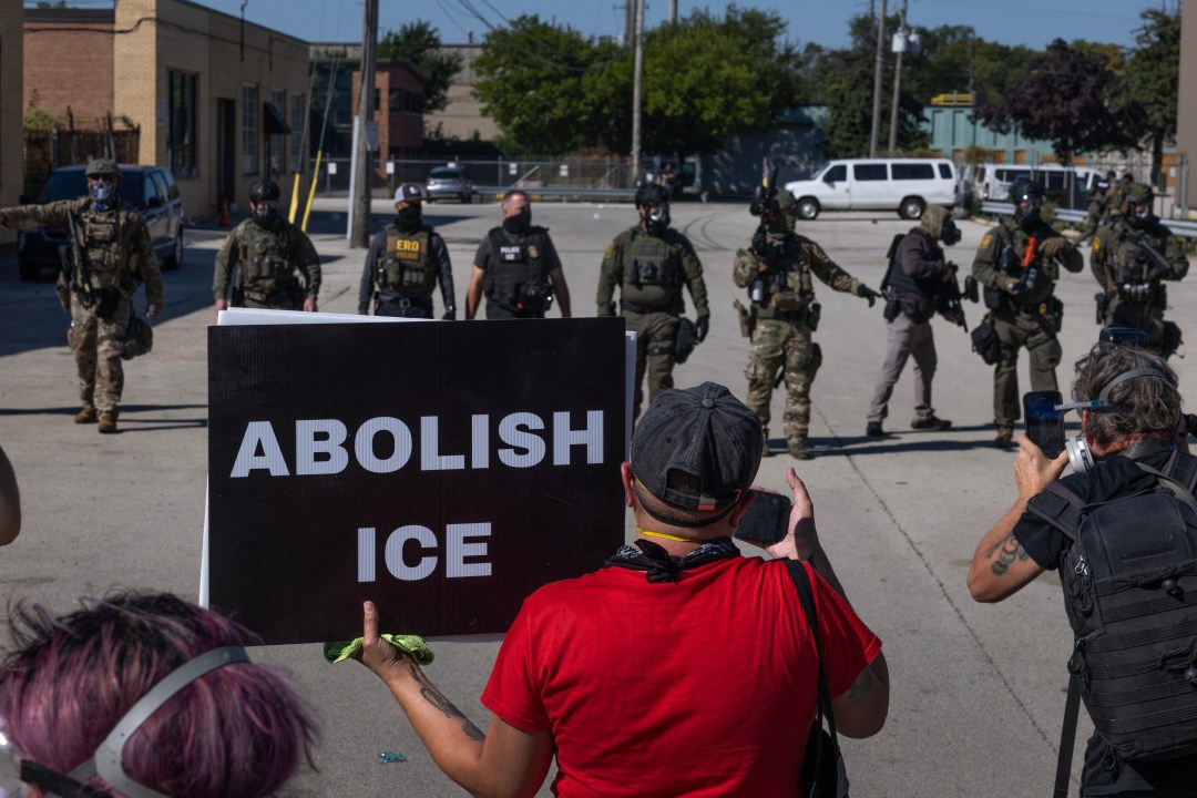 Five cities hit with federal presence remain on edge - justice - iustitia. Bg Protesters gather in front of ice officers. One holds a sign reading abolish ice