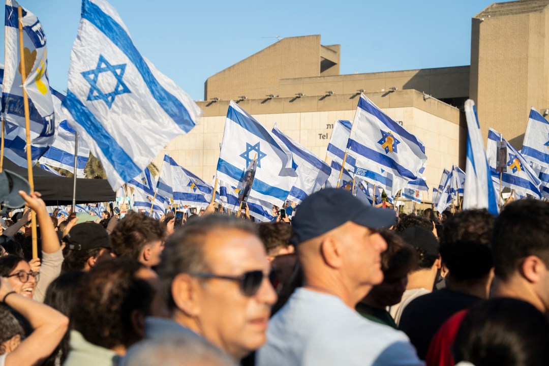 Crowd holding israeli flags watches live broadcast of israeli hostages being released from gaza