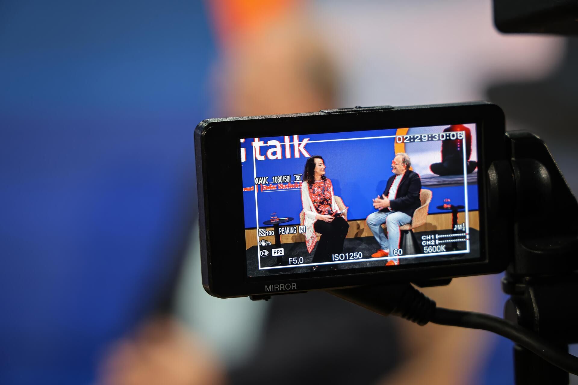 Kameradisplay zeigt eine aufgezeichnete gesprächsszene mit moderatorin und gast.