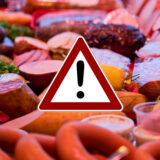 Ein Wurst-Theke in einem Supermarkt, darüber ein rotes Warndreieck