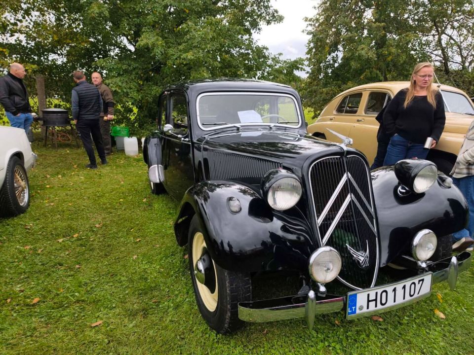 Juodas senovinis „citroën“ automobilis ir parodos lankytojai rudaminoje.