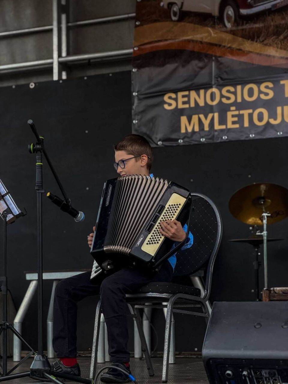 Jaunasis atlikėjas groja akordeonu senosios technikos mylėtojų šventės scenoje.