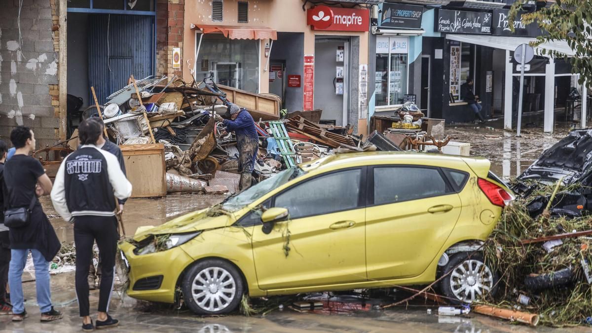 Varias personas quitan el barro de las calles mientras se acumula el mobiliario que han tenido que sacar debido a las inundaciones en els poblets.
