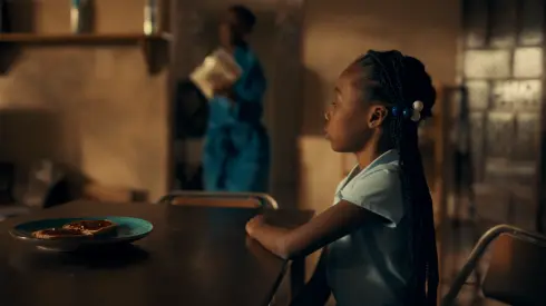 A young girl sits at the dining room table in a still from the "three colors: pan-african" film.
