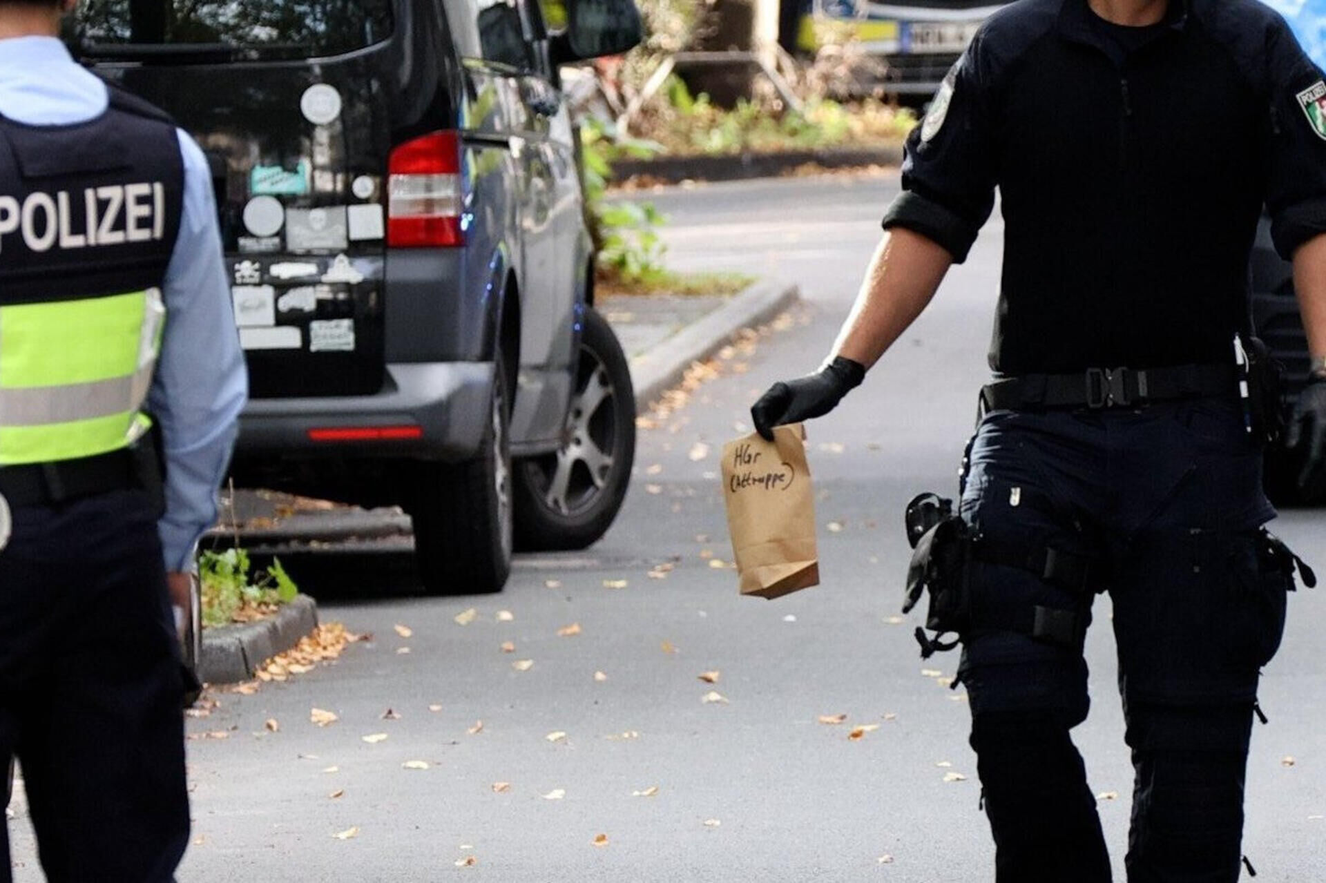 Nach häftlingsbefreiung in essen: justizminister limbach will überfallene beamte besuchen 2026 - iustitia. Bg - gerechtigkeit Ein polizist hält eine papiertüte in der hand. Zwei unbekannte haben mitten in essen zwei justizbeamte angegriffen und einen 34 jahre alten häftling befreit.