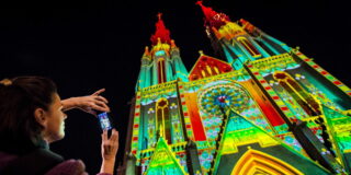 Nur 90 minuten von nrw entfernt: das schönste lichterfestival der niederlande 2026 - iustitia. Bg - gerechtigkeit Eine frau fotografiert eine kirche in eindhoven, die zum lichterfestival glow bunt angeleuchtet wird.