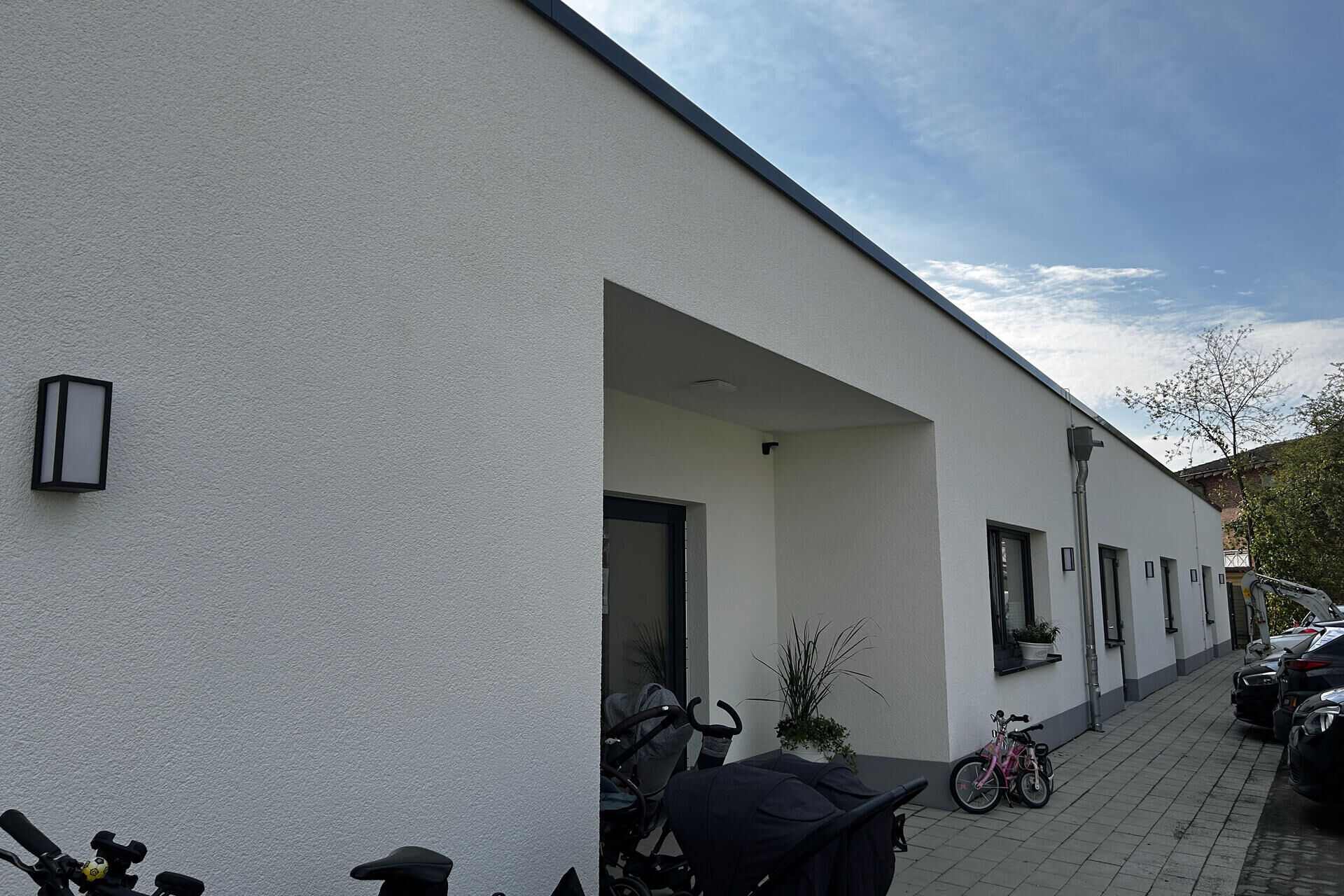 Der Kindergarten St. Konrad - Die Weltenentdecker von Außen. Im Eingangsbereich steht ein Kinderfahrrad und ein Kinderwagen vor der weißen Hausfassade.