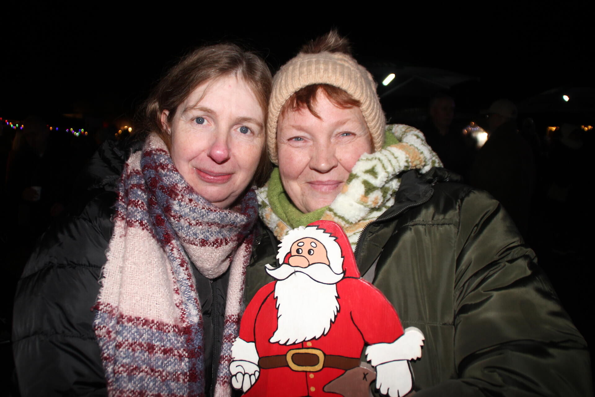Zwei frauen stehen auf dem weihnachtsmarkt im volkspark brambauer eng beieinander und lächeln in die kamera. Sie tragen warme winterjacken und schals und halten eine weihnachtsmannfigur vor sich.